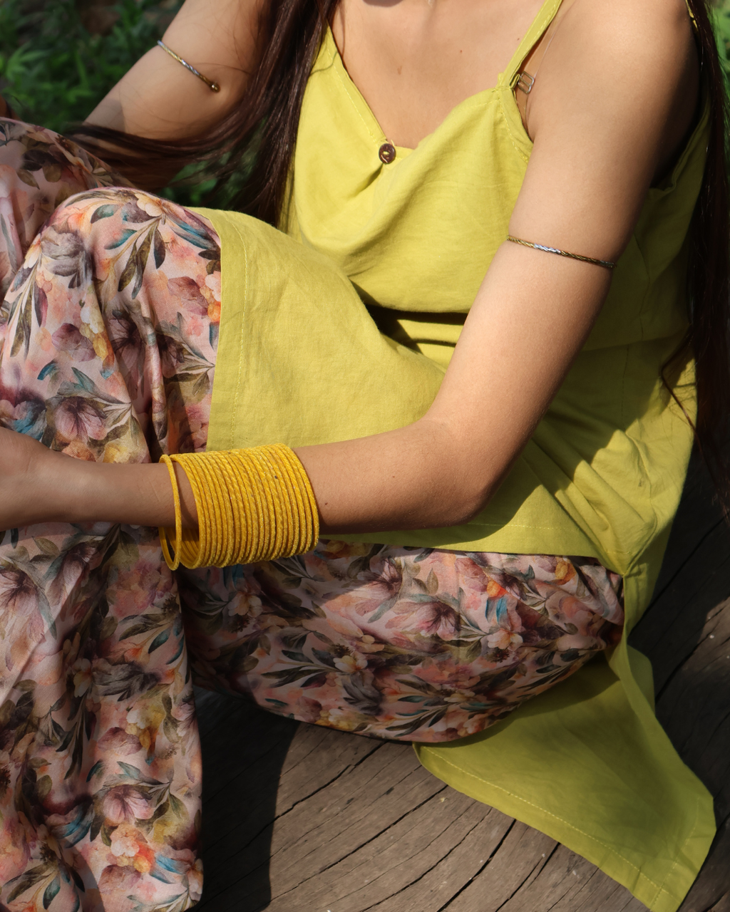 Person wearing a yellow top and floral skirt with a yellow bracelet.