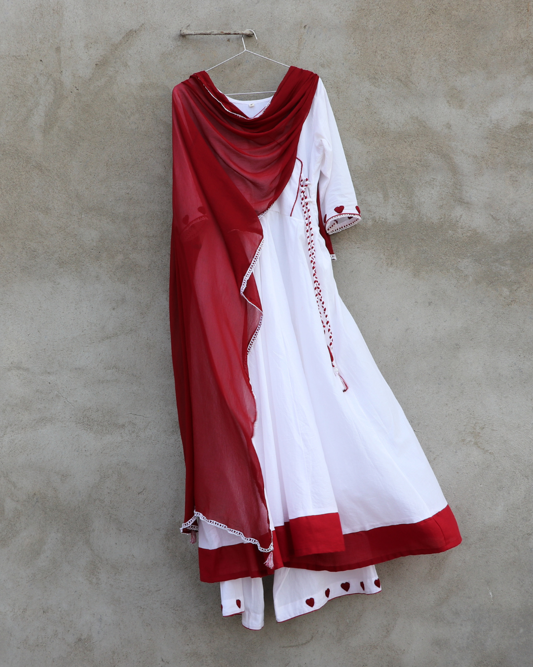 Red and white dress with lace details on a hanger against a beige wall
