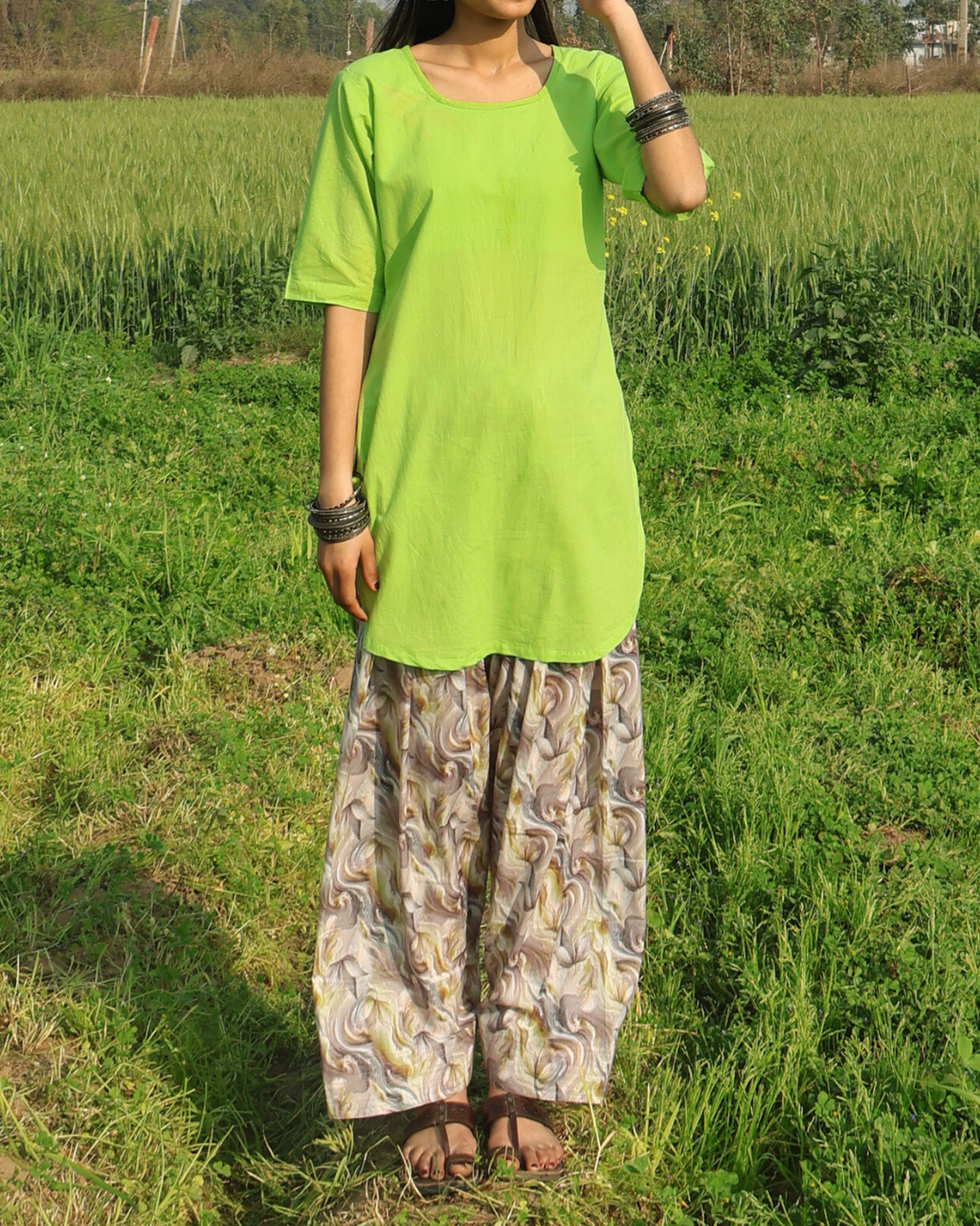 Person wearing a bright green top and patterned pants standing in a grassy field.
