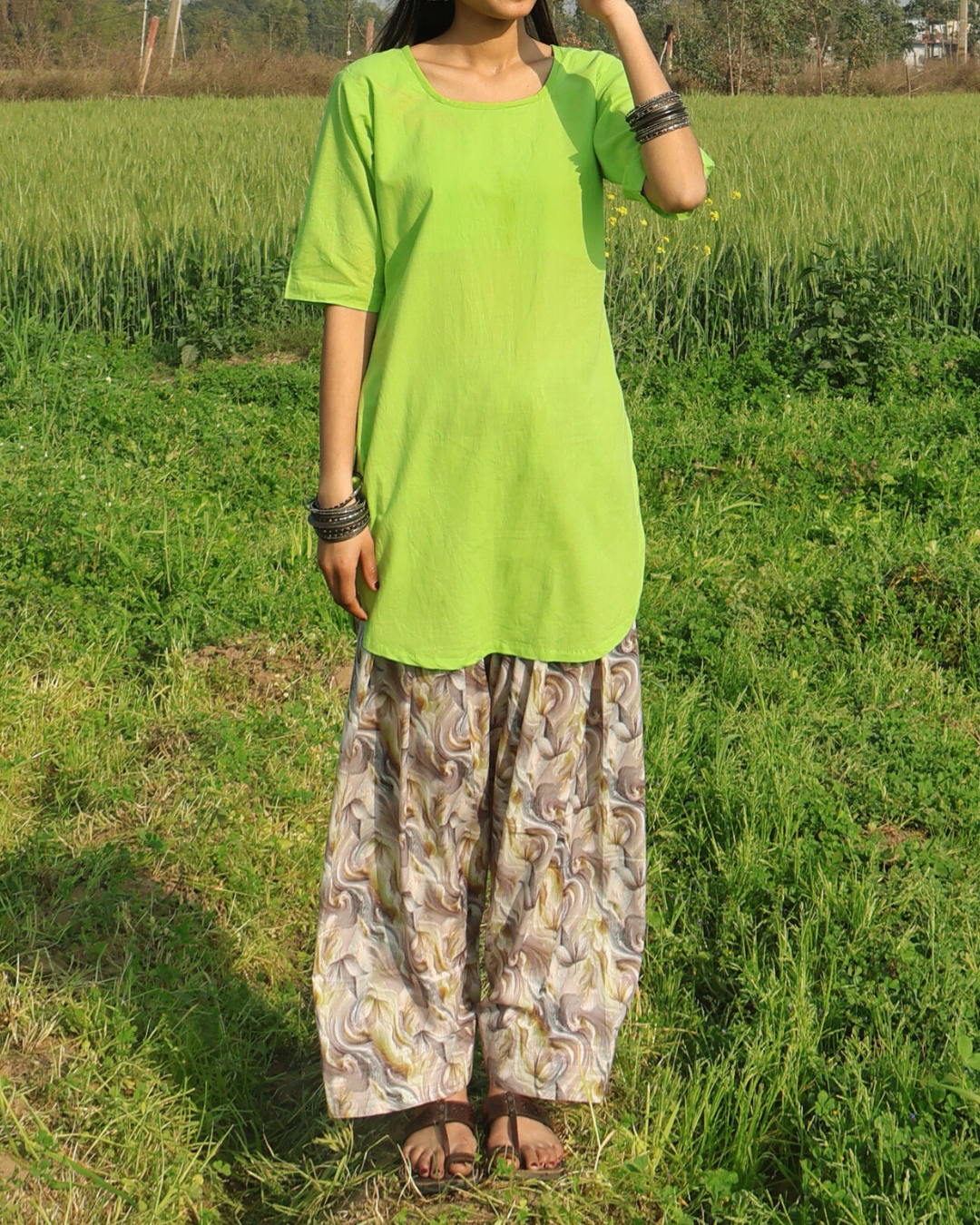 Person wearing a bright green top and patterned pants standing in a grassy field.