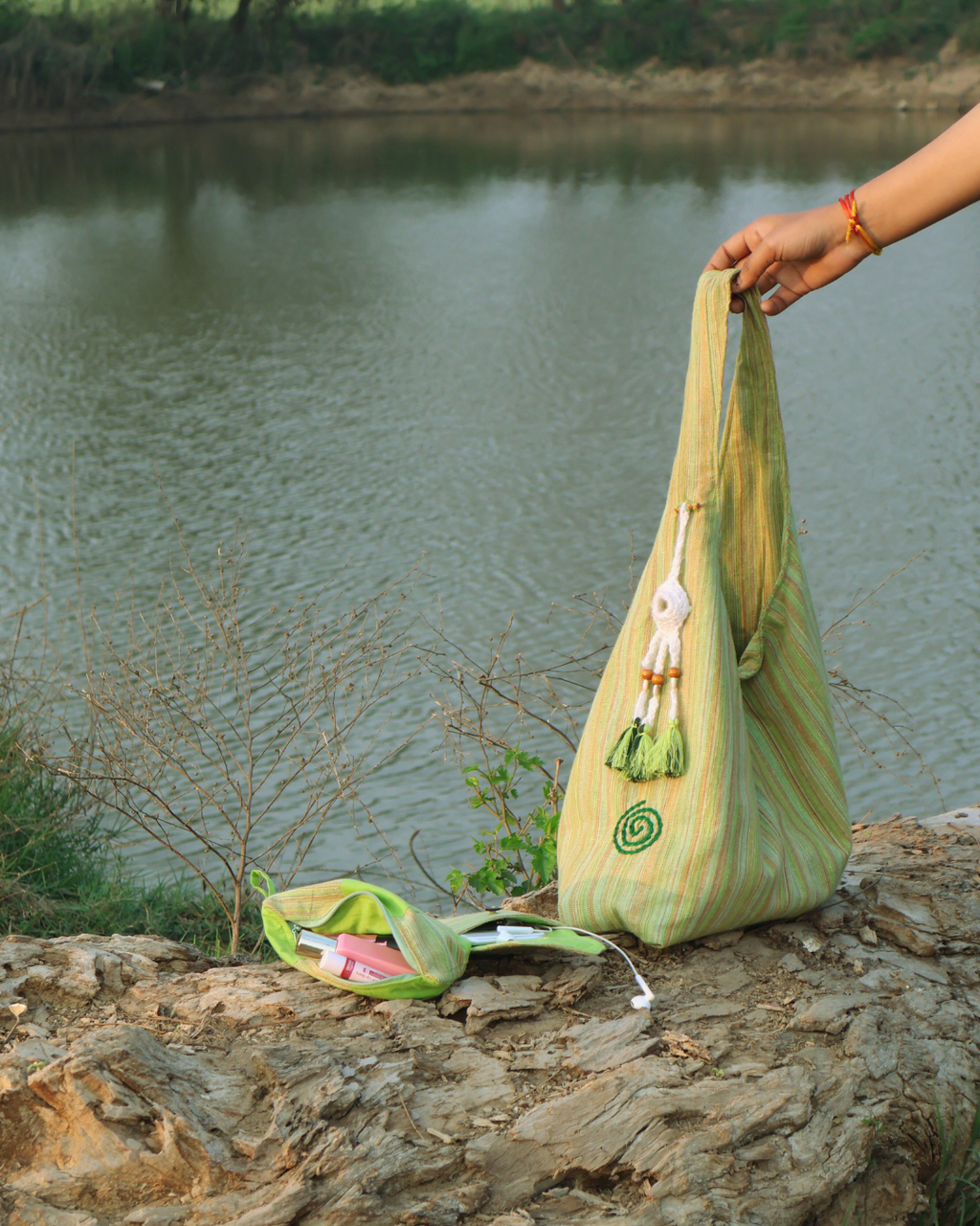Green handbag with a decorative element on a stone surface near a body of water.