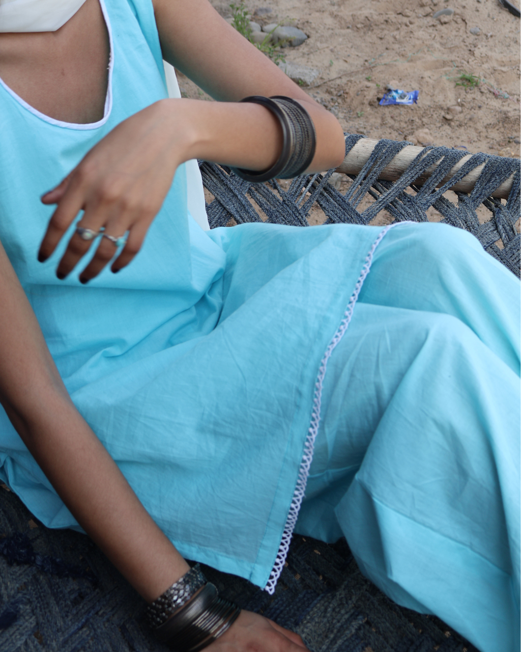 Person wearing a light blue outfit with white trim sitting on a woven chair.