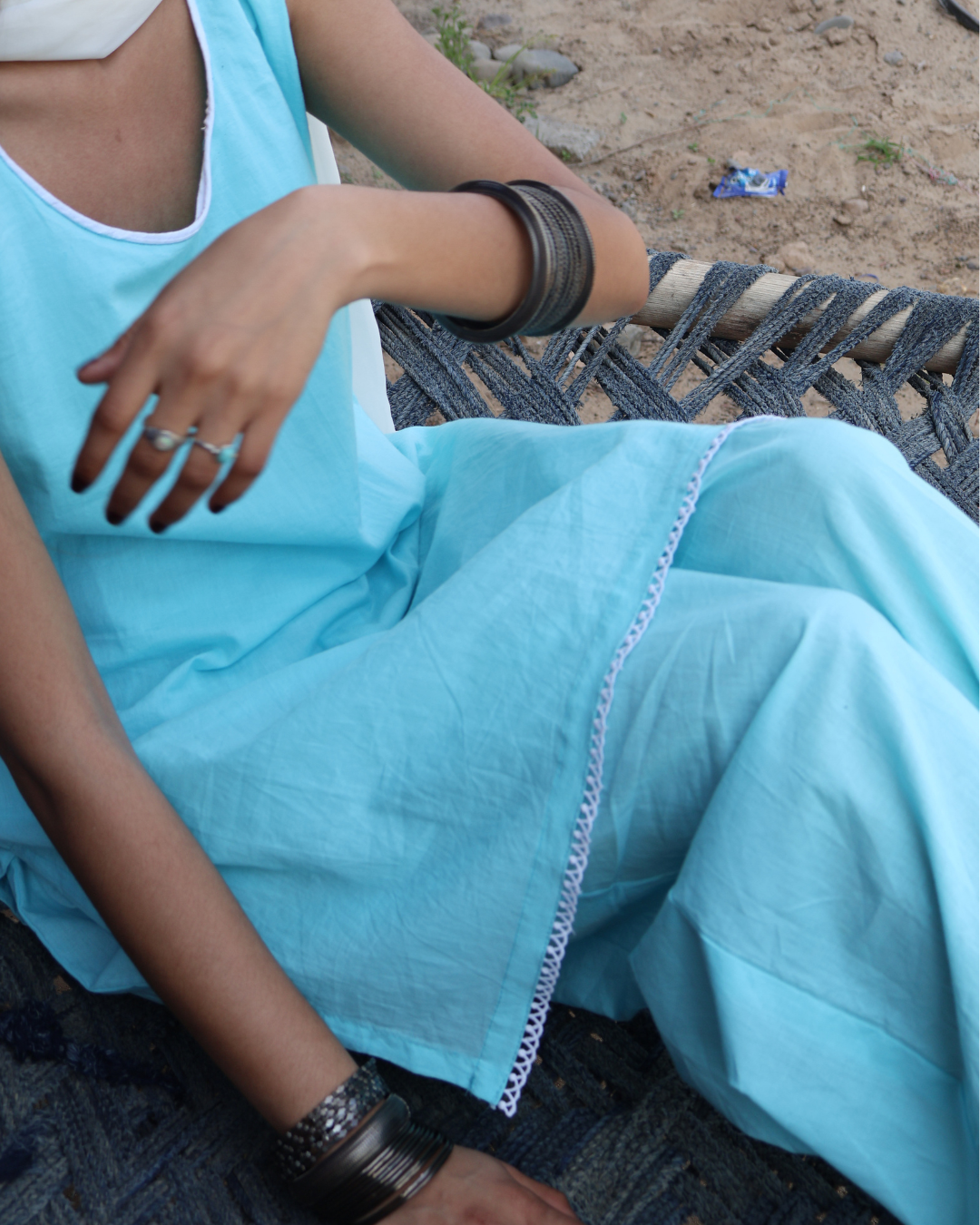 Person wearing a light blue outfit with white trim sitting on a woven chair.