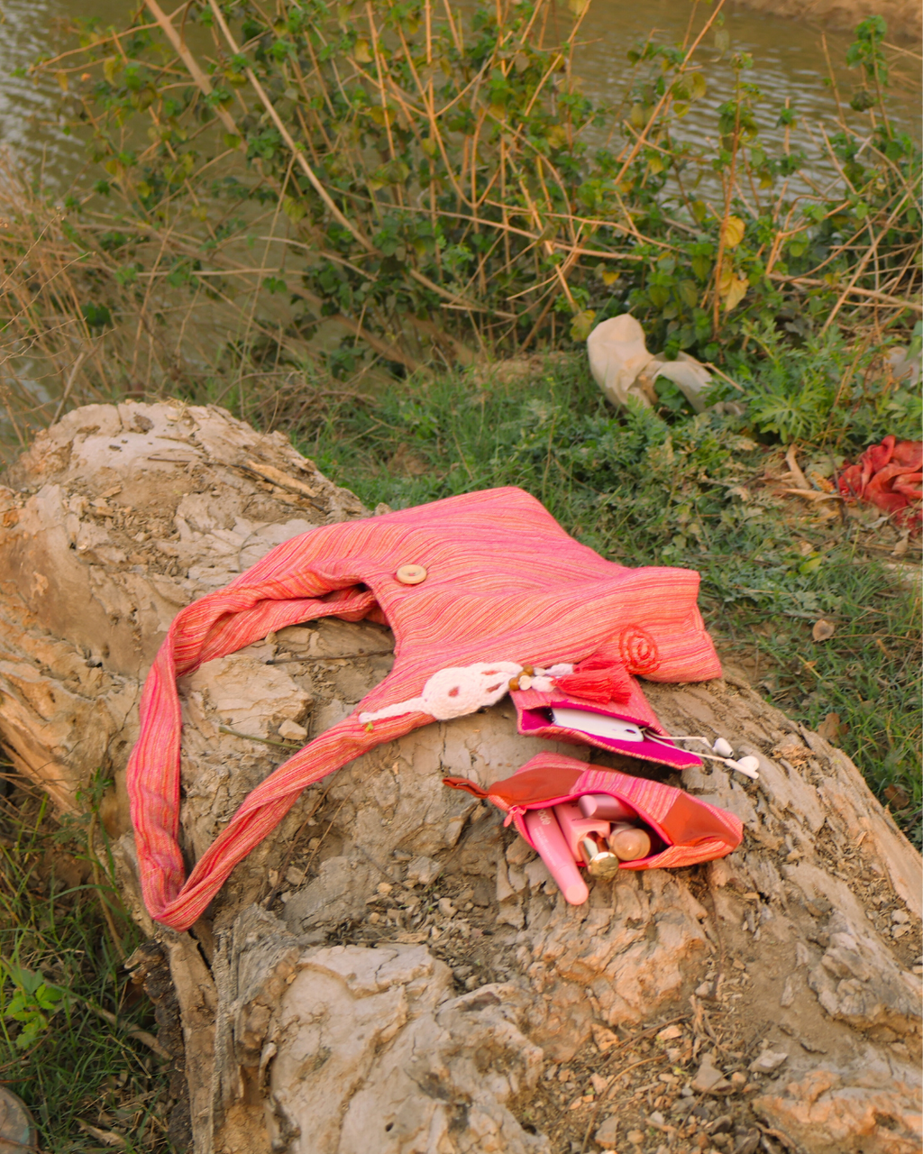 Pink garment with a doll on a rocky surface near water and plants