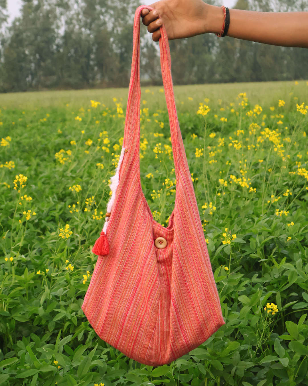 Pink handbag with a tassel held by a hand in a field of yellow flowers.