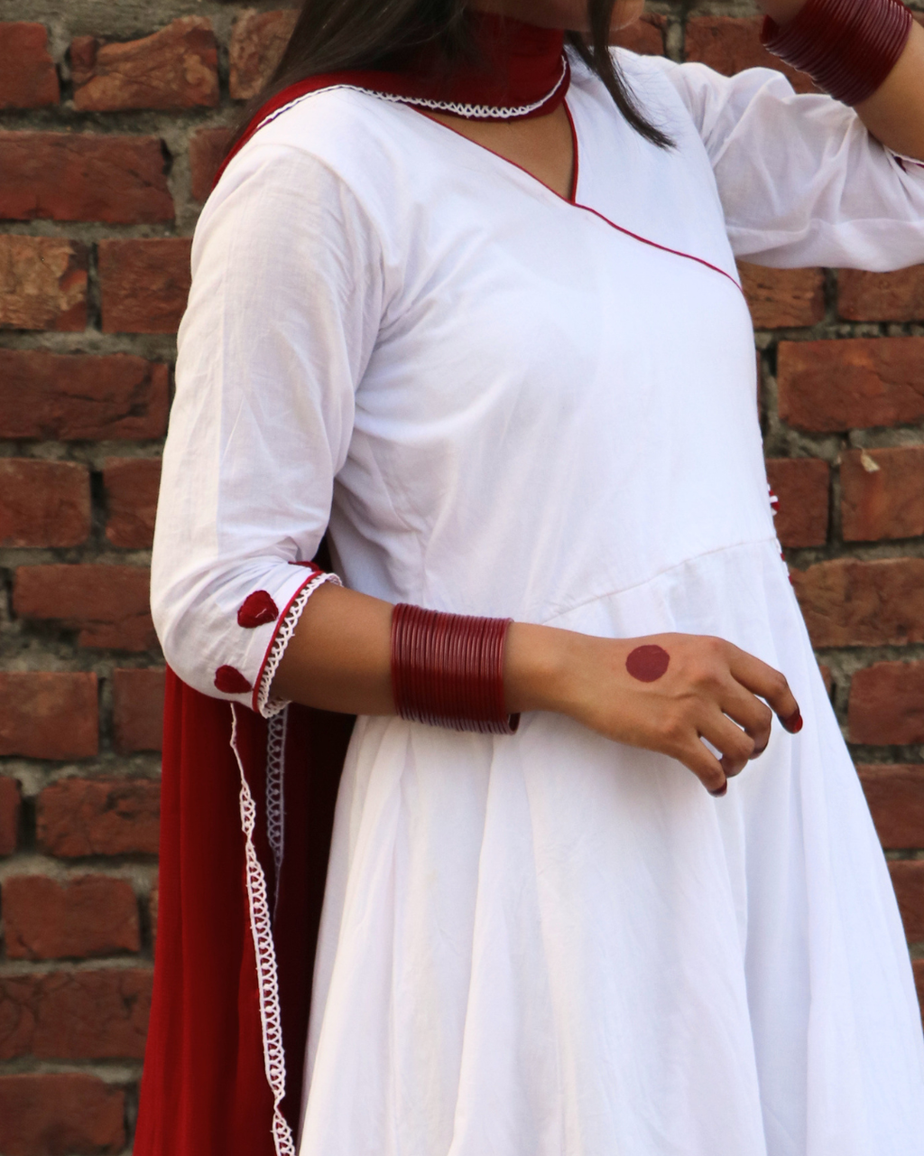 Person wearing a white outfit with red accents against a brick wall.