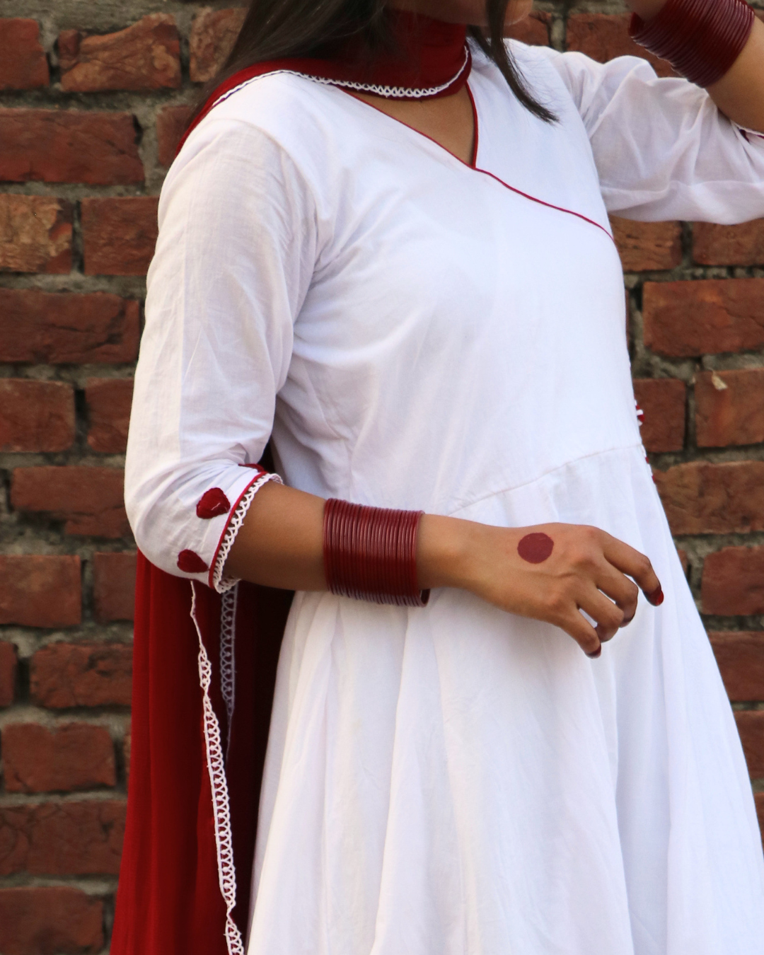 Person wearing a white outfit with red accents against a brick wall.