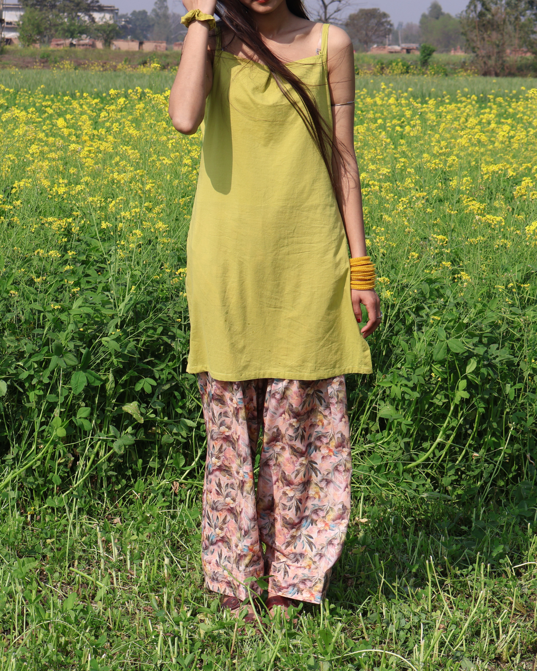 Woman in a yellow dress and floral pants standing in a field of yellow flowers.