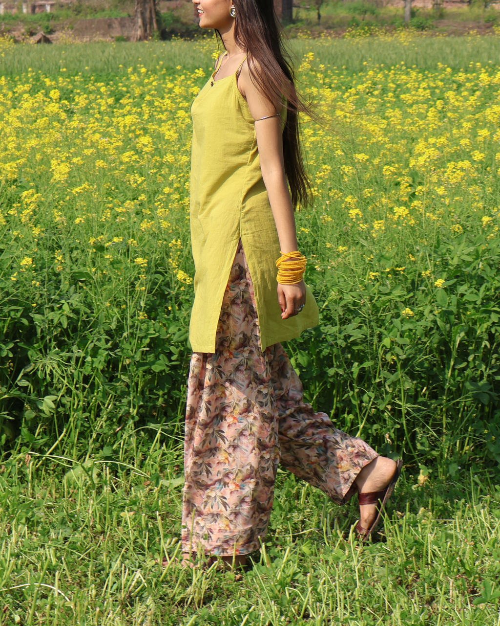 Woman in a yellow top and patterned pants standing in a field of yellow flowers.