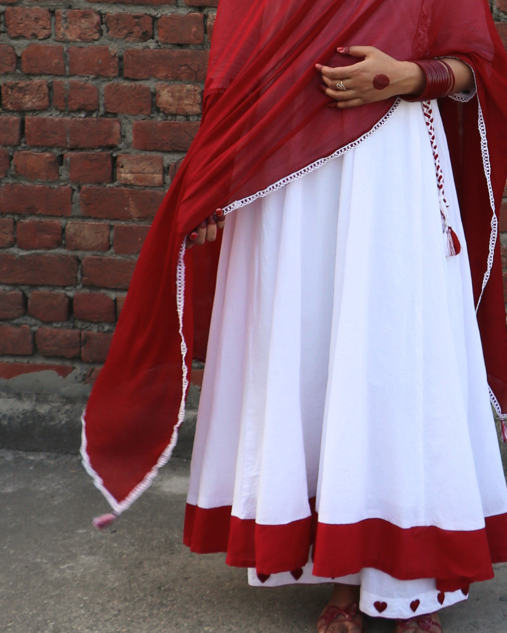 Person wearing a red and white traditional outfit against a brick wall.