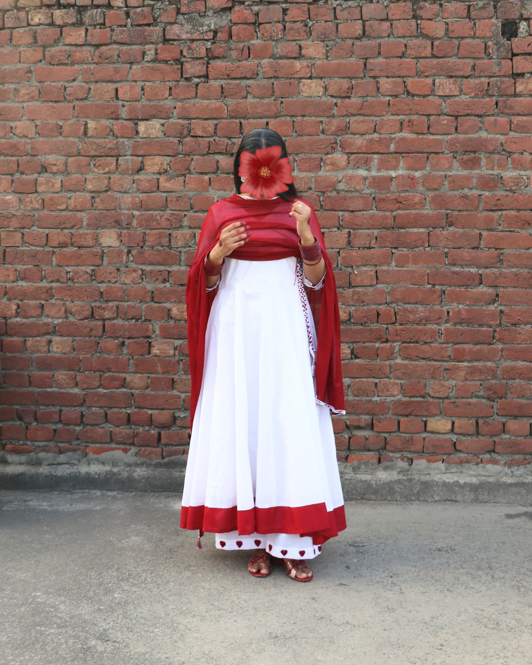 Person wearing a white dress with red accents against a brick wall.