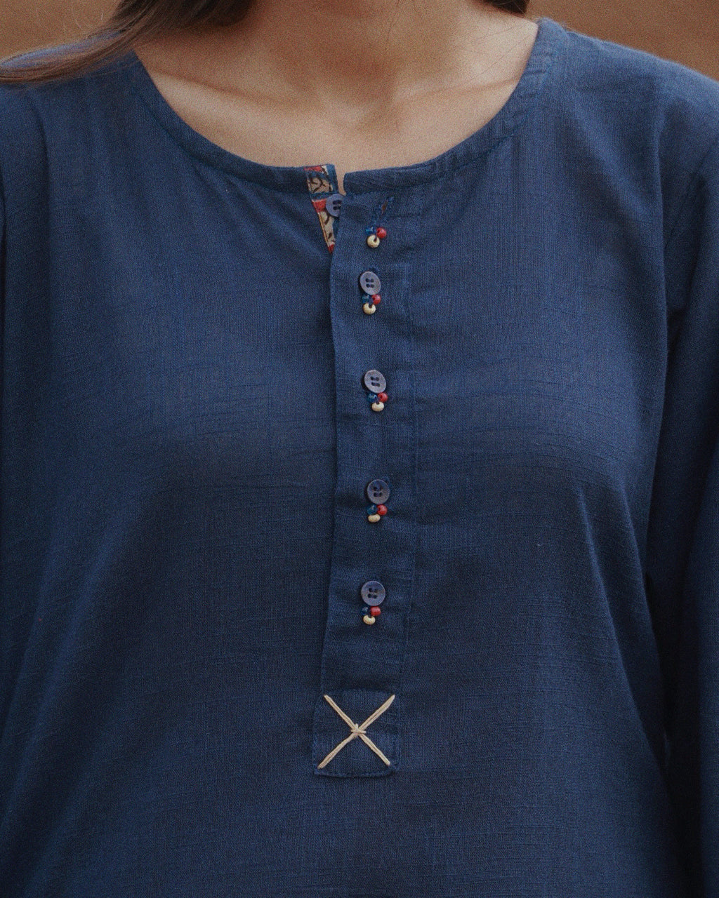 Close-up of a person wearing a dark blue long-sleeve kurta with a round neckline, button placket, and small embroidered detail near the hem.