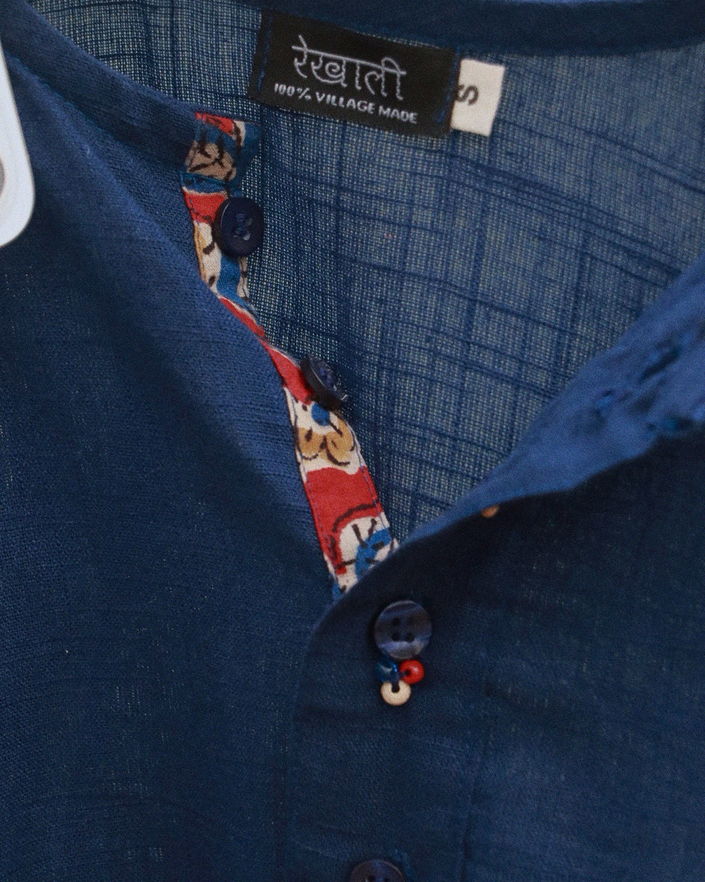 Close-up of a dark blue textured shirt with a patterned inner placket and a black brand label reading 'Rekhali'.