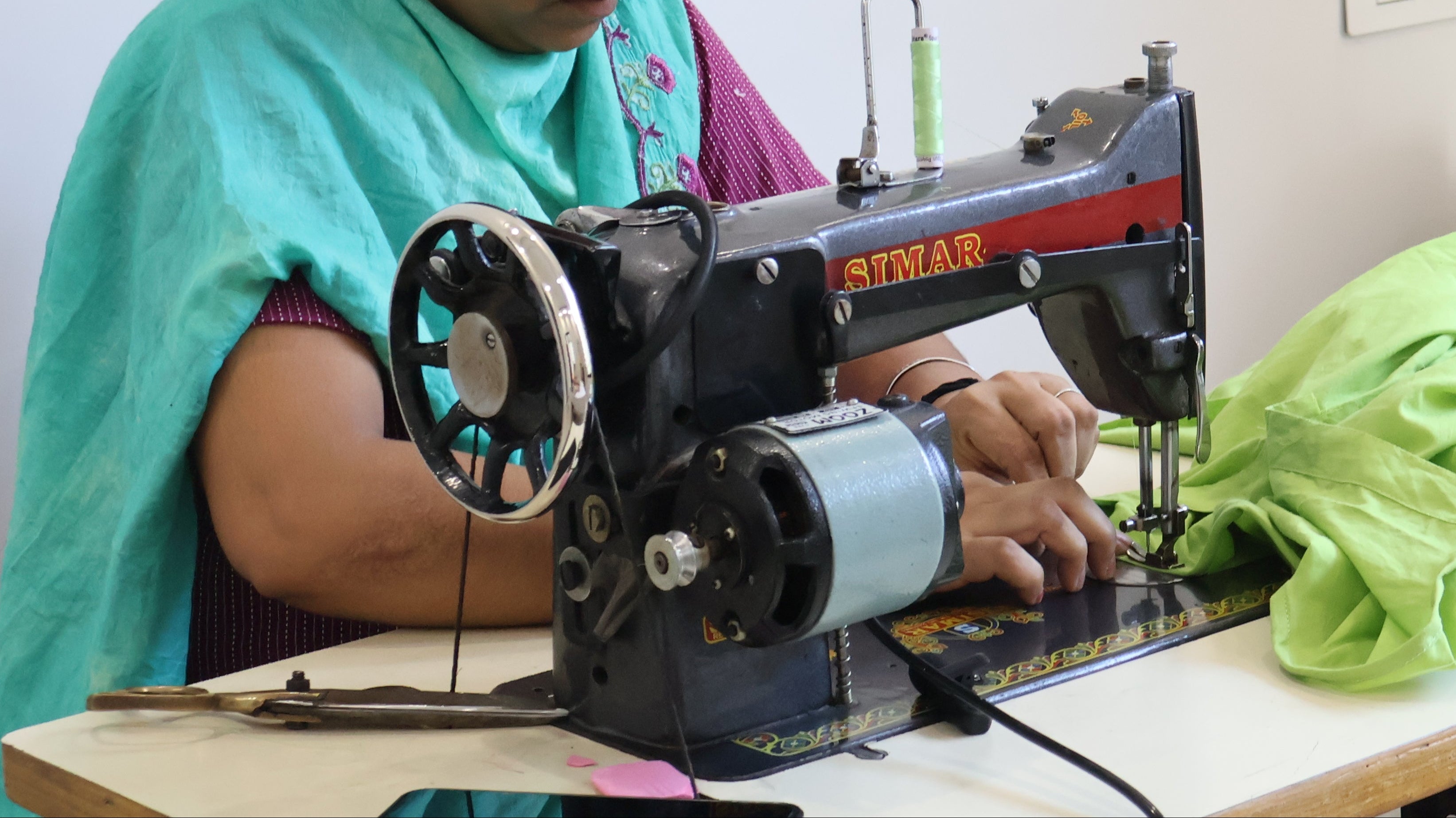 Woman working on a sewing machine with green fabric in a room.